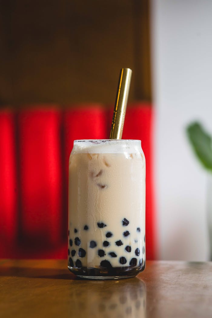 Close-up of ice-cold milk tea with tapioca pearls and gold straw on a table.